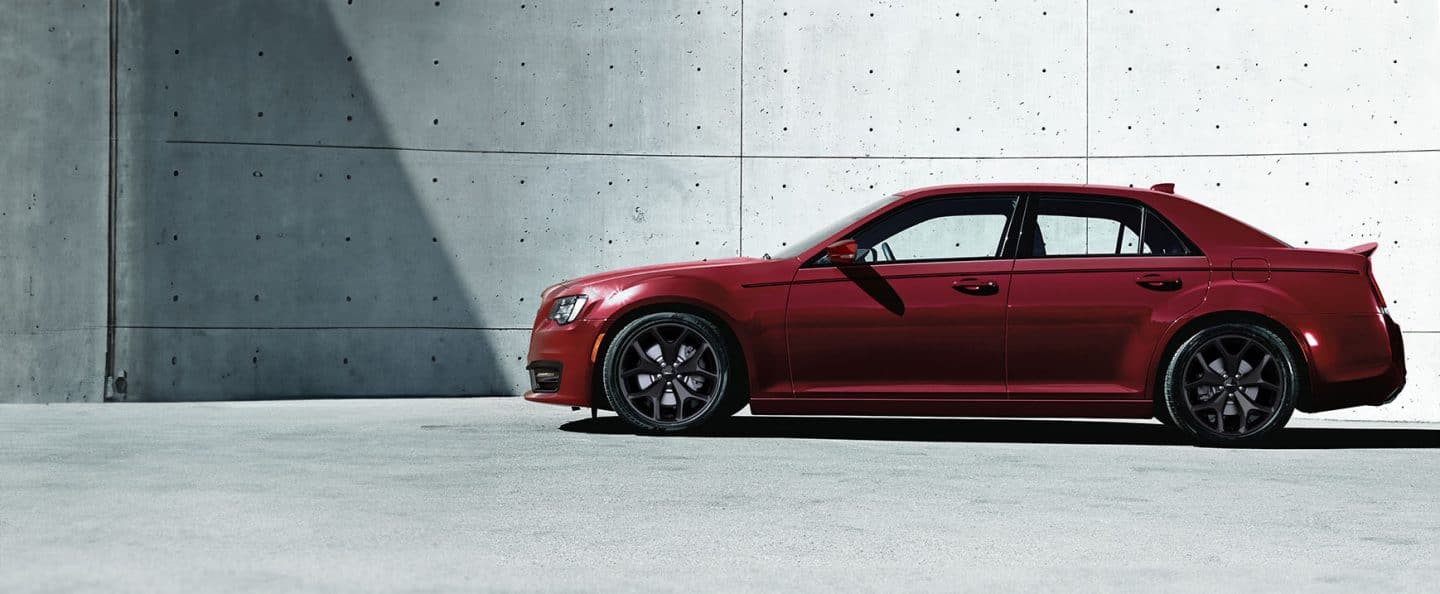 A driver-side profile of a red 2023 Chrysler 300S V8 parked next to a cement wall.