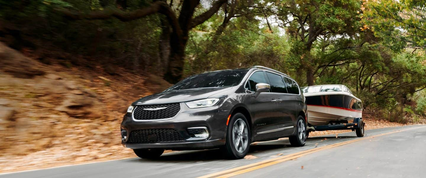 The 2023 Chrysler Pacifica Pinnacle towing a motorboat on a two-lane road.