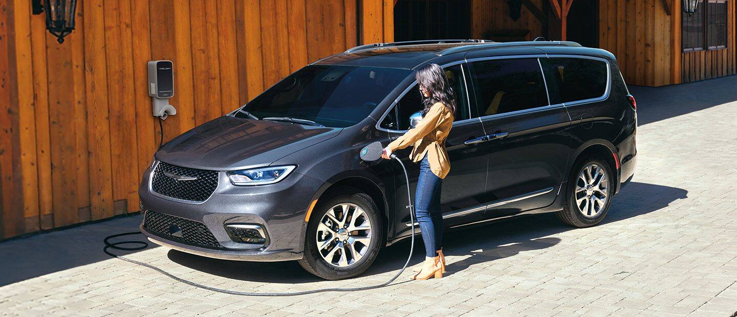 Una mujer enchufa un cable de carga en el puerto de carga de una Chrysler Pacifica Pinnacle Hybrid 2023.