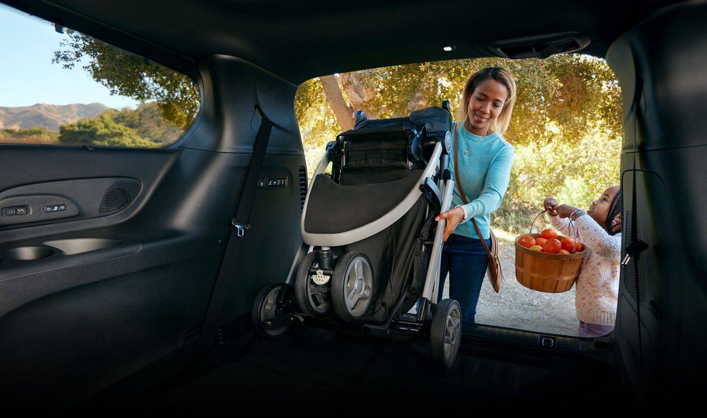 Una mujer saca un cochecito plegado de la zona de carga de una Chrysler Pacifica Hybrid 2023.