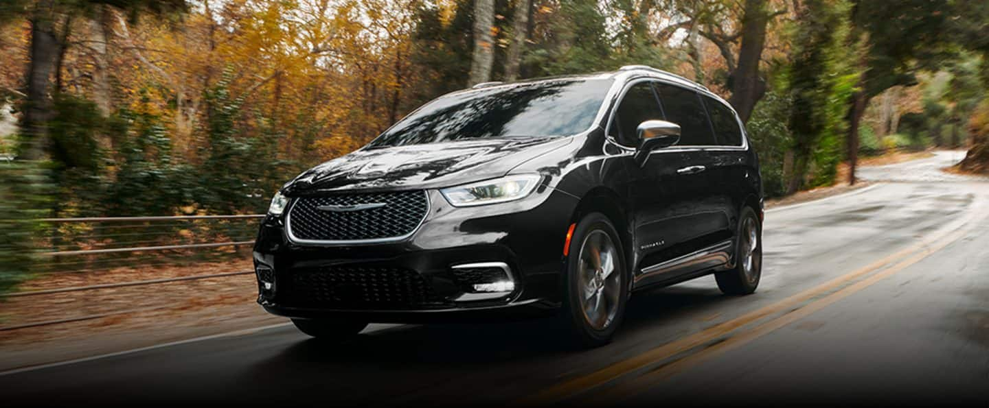 An angled driver-side profile of the 2024 Chrysler Pacifica Pinnacle being driven down a country road, the background is blurred to indicate the vehicle is in motion.