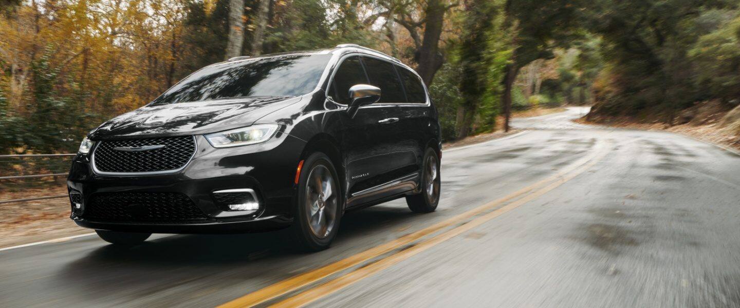 Una Chrysler Pacifica Pinnacle AWD 2023 circulando por un camino rural sinuoso. El fondo está borroso para indicar la velocidad del vehículo.