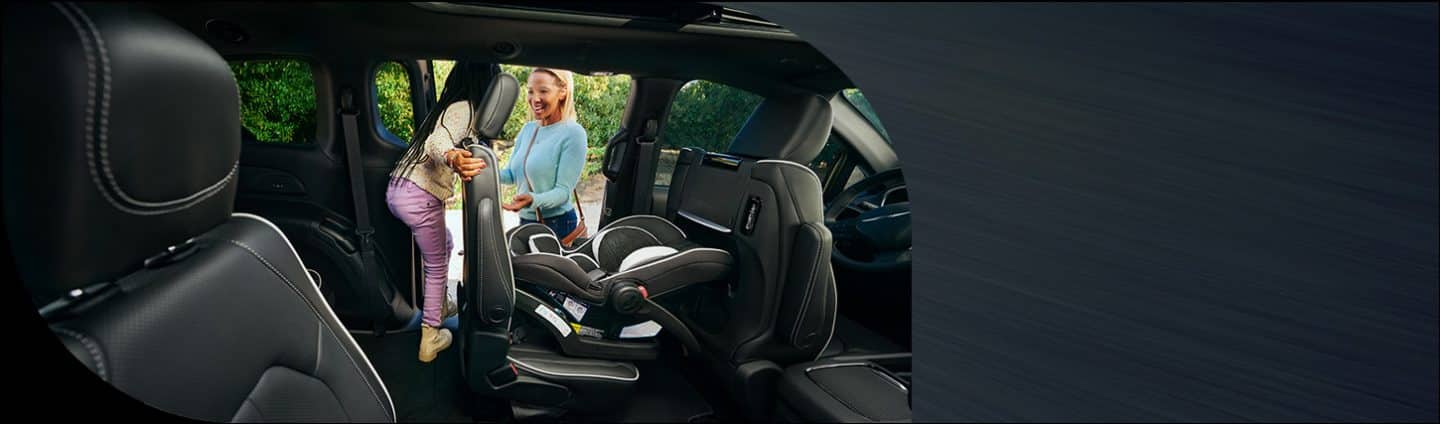 The driver-side second-row seat with an infant seat attached in the 2026 Chrysler Pacifica Limited. The seat is tilted forward so a child can exit the third row through the sliding door.