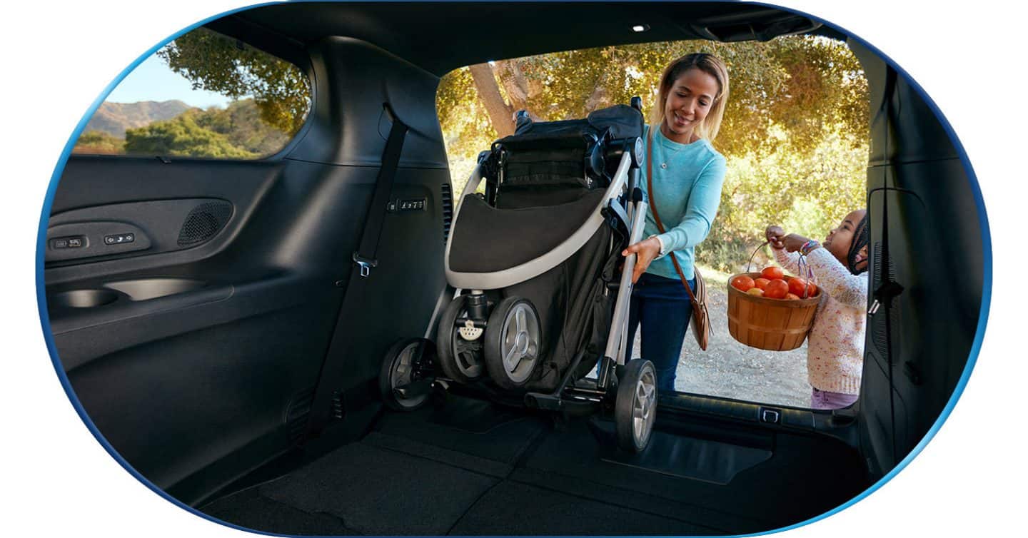 A  woman pulling a collapsed stroller out of the cargo area of a 2026 Chrysler Pacifica Hybrid.