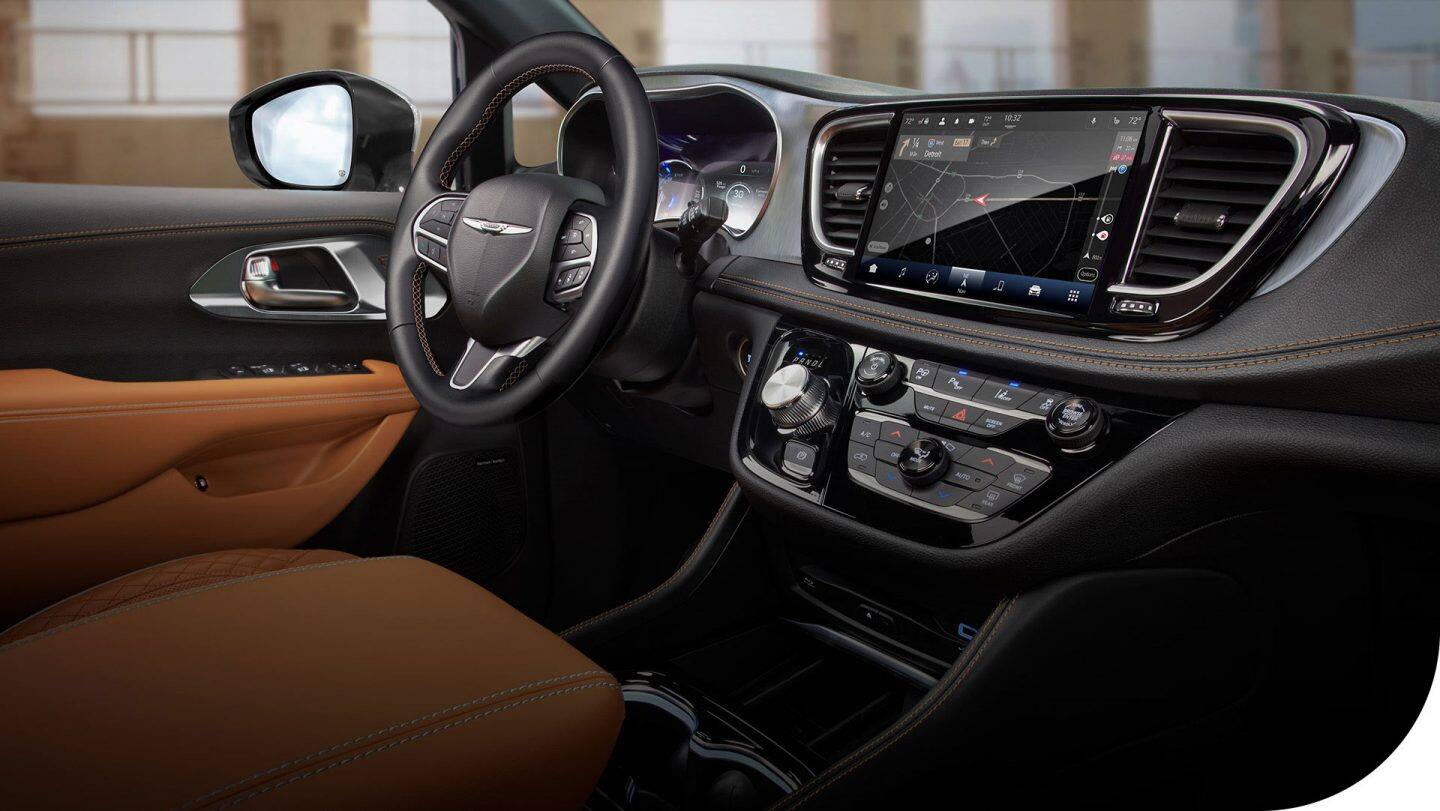 La fila delantera de la Chrysler Pacifica Plug-in Hybrid Pinnacle 2026, incluidos los asientos, el volante, la pantalla digital del panel de instrumentos, la pantalla táctil Uconnect y los controles de la consola central.