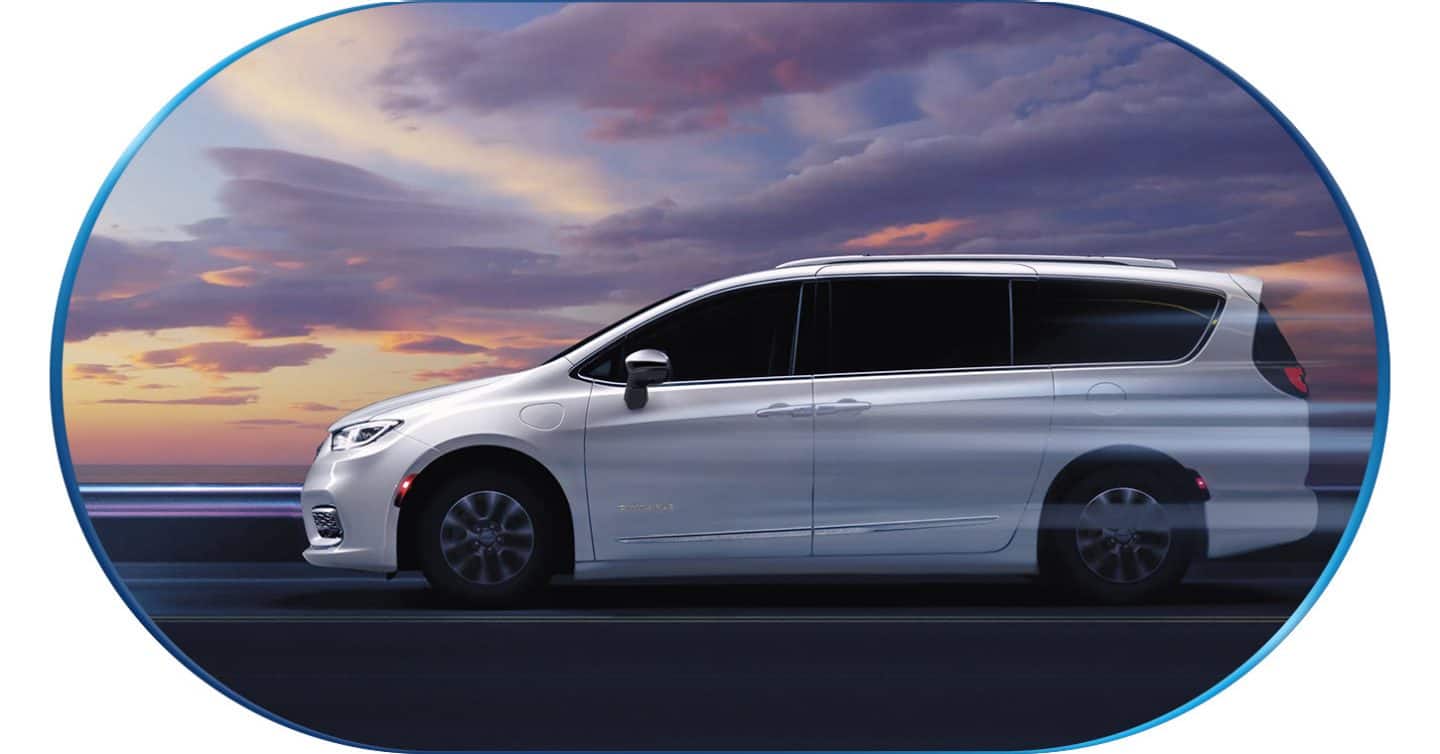 A driver-side profile of a white 2026 Chrysler Pacifica Plug-in Hybrid Pinnacle with its wheels blurred to indicate the vehicle is in motion.