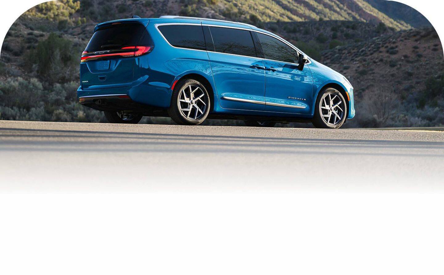 Ángulo trasero del lado del pasajero de una Chrysler Pacifica Pinnacle 2027 azul en un camino de montaña.