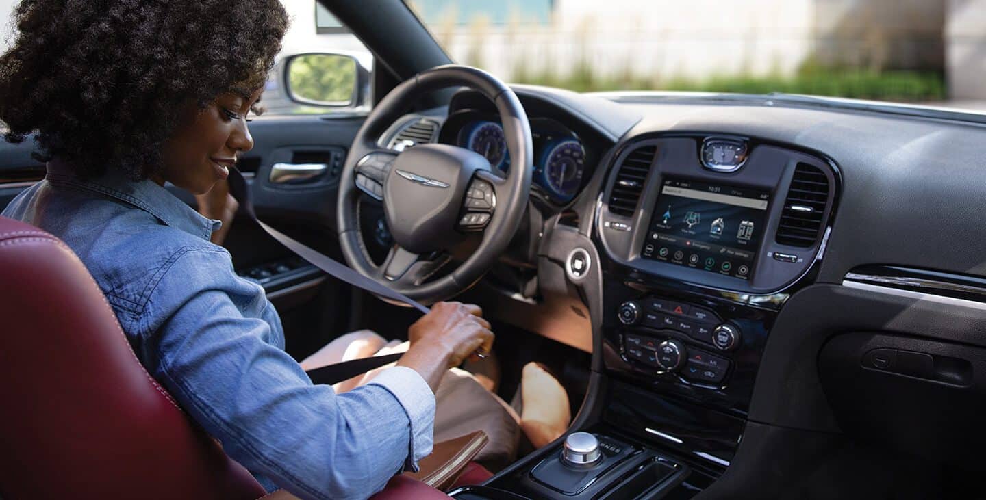 Display A driver at the wheel of the 2021 Chrysler 300S V6, fastening her seatbelt.