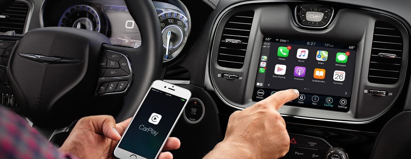 A driver holding a smartphone and reaching for the touchscreen in the 2021 Chrysler 300, displaying connectivity icons.