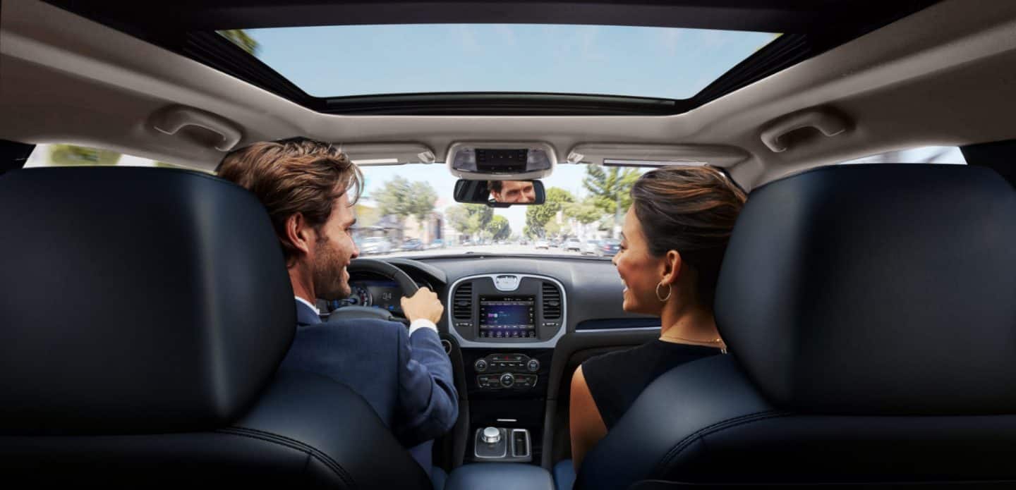 Display The interior of the 2023 Chrysler 300 with a driver and front passenger talking to each other in the front seats.