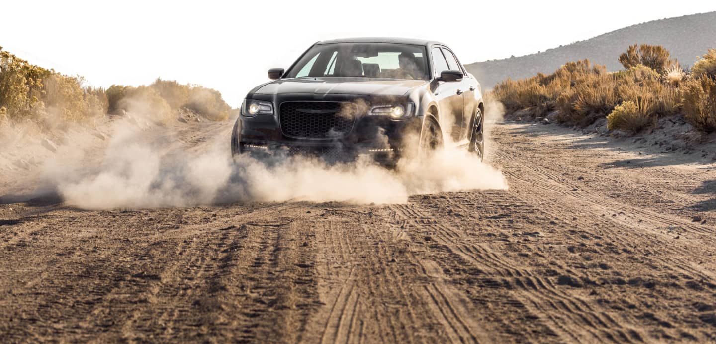 The 2023 Chrysler 300 with a cloud of dust coming from its wheels as it's driven on a dirt road.