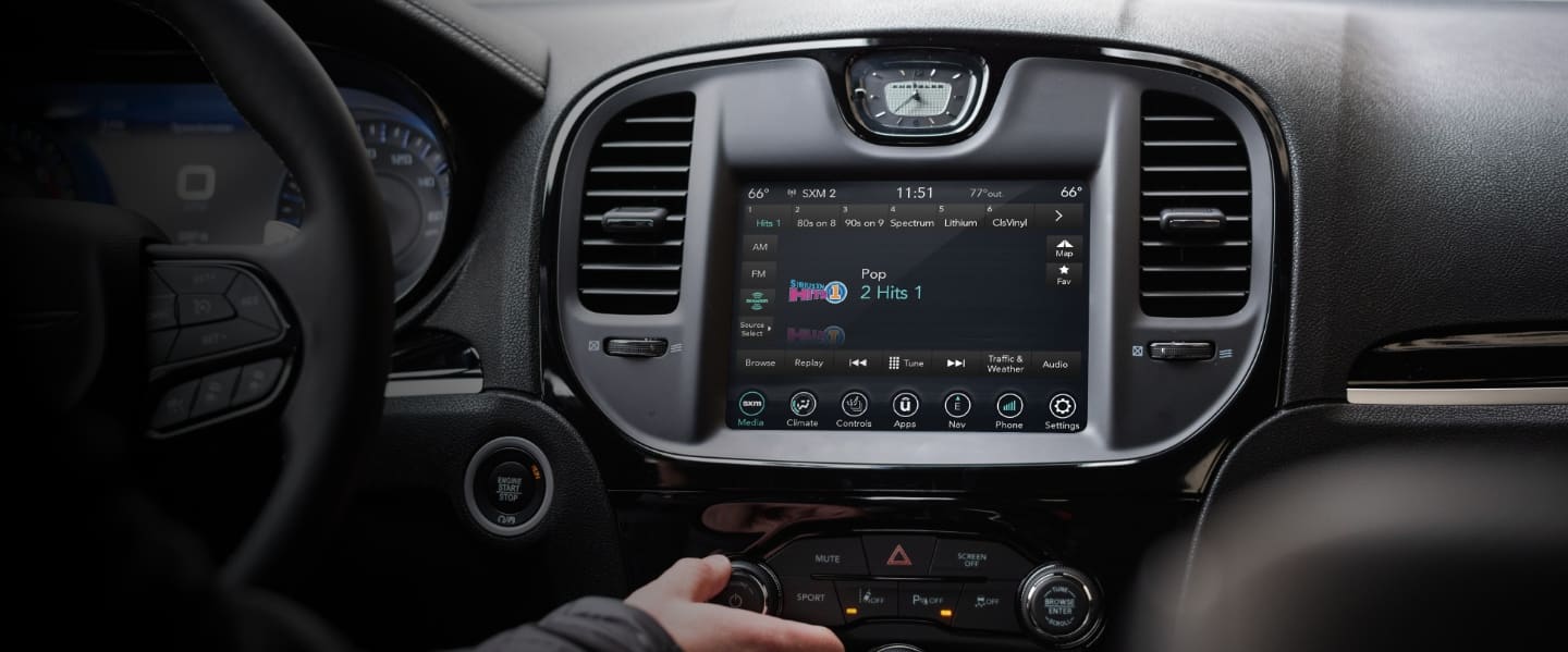 A close-up of the touchscreen in the 2023 Chrysler 300 with a driver's hand reaching for the controls below it.