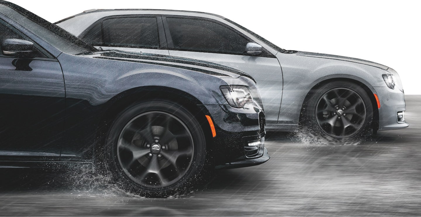 Two 2023 Chrysler 300 models being driven on a wet, rainy road, with water spraying from the wheels.