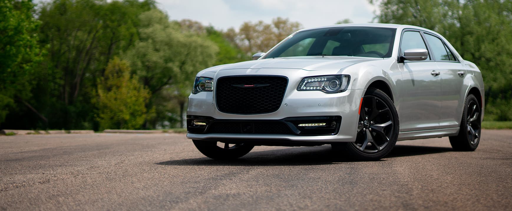 A rear angle of a 2023 Chrysler Pacifica Limited with the S Appearance Package being driven on a country road. The background is blurry indicating the vehicle is in motion. 