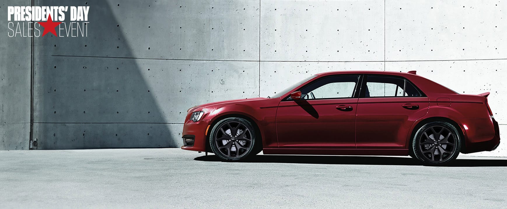 A driver-side profile of a red 2023 Chrysler 300S V8 parked next to a cement wall.
