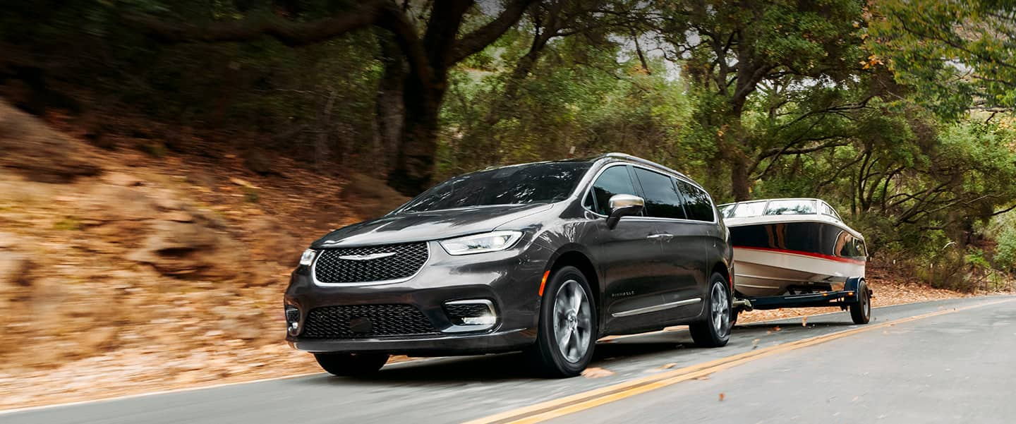 The 2023 Chrysler Pacifica Pinnacle towing a motorboat on a two-lane road.