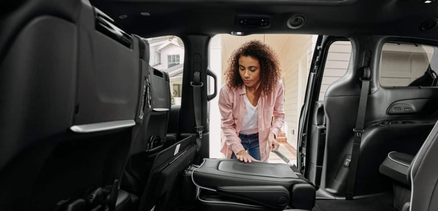 Display A woman standing at the open sliding side door in the 2023 Chrysler Pacifica Limited with the S Appearance Package, folding down the seatback of the second-row passenger-side seat.