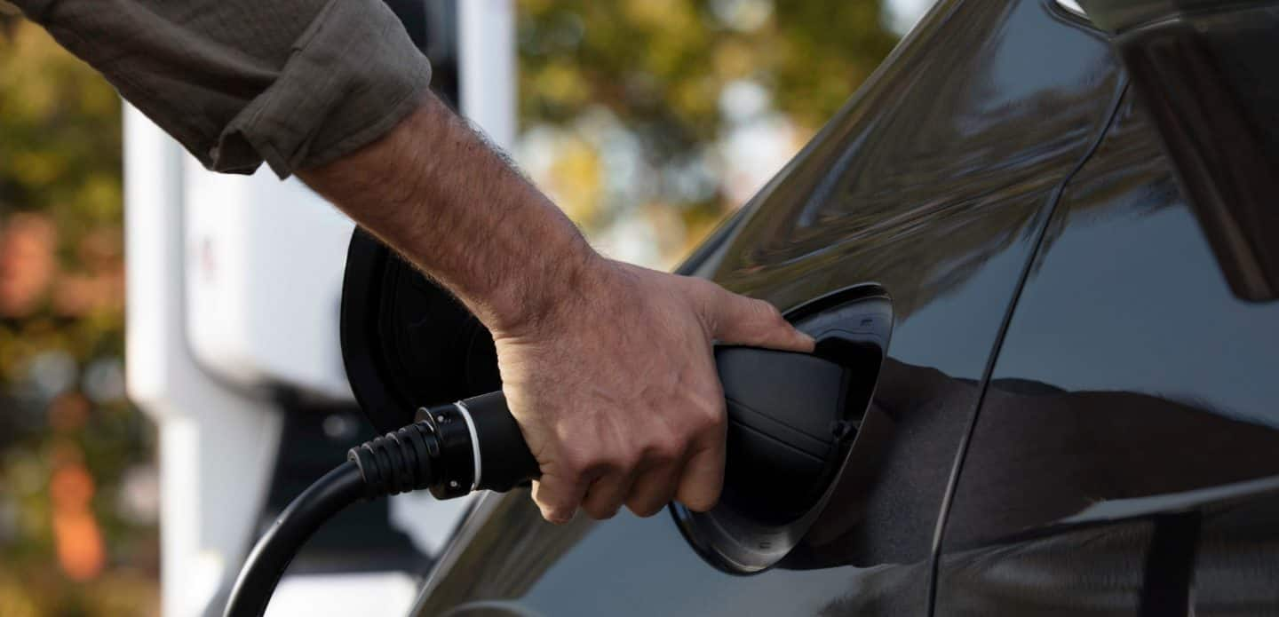 Display A man plugging a charging cord into the charging port on the 2023 Chrysler Pacifica Hybrid.