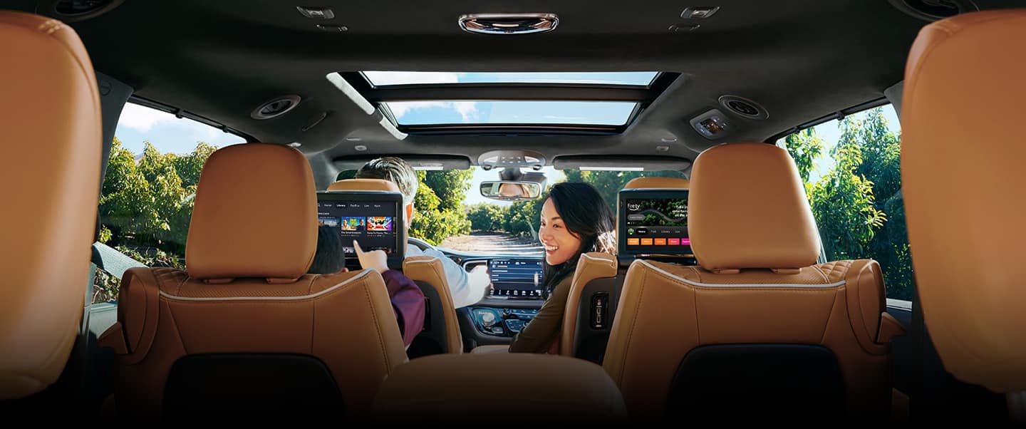 The interior of the 2023 Chrysler Pacifica Pinnacle Hybrid with a man driving and a woman looking back at a boy in the second row that is playing a game on the seatback-mounted touchscreen.