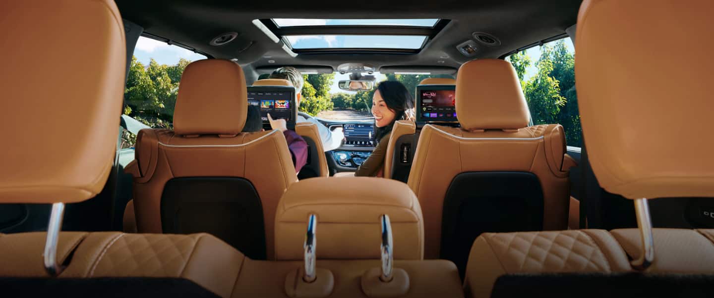 The interior of the 2023 Chrysler Pacifica Pinnacle Hybrid with a man driving and a woman looking back at a boy in the second row that is playing a game on the seatback-mounted touchscreen.