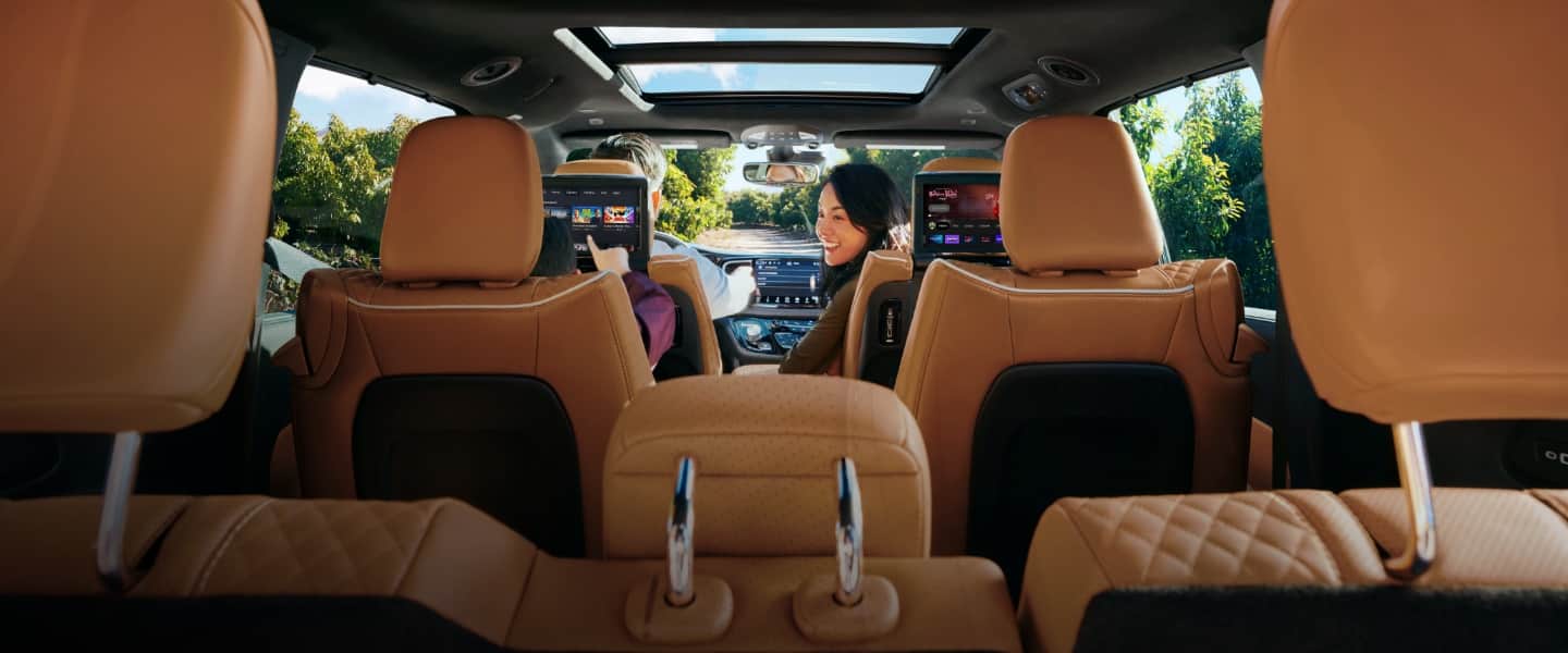 The interior of the 2023 Chrysler Pacifica Pinnacle with a man driving and a woman looking back at a boy in the second row that is playing a game on the seatback-mounted touchscreen.