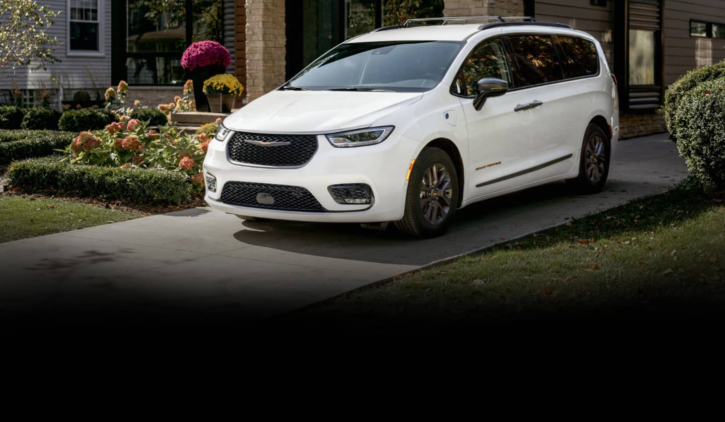 A white 2023 Chrysler Pacifica Road Tripper Hybrid parked in a residential driveway.