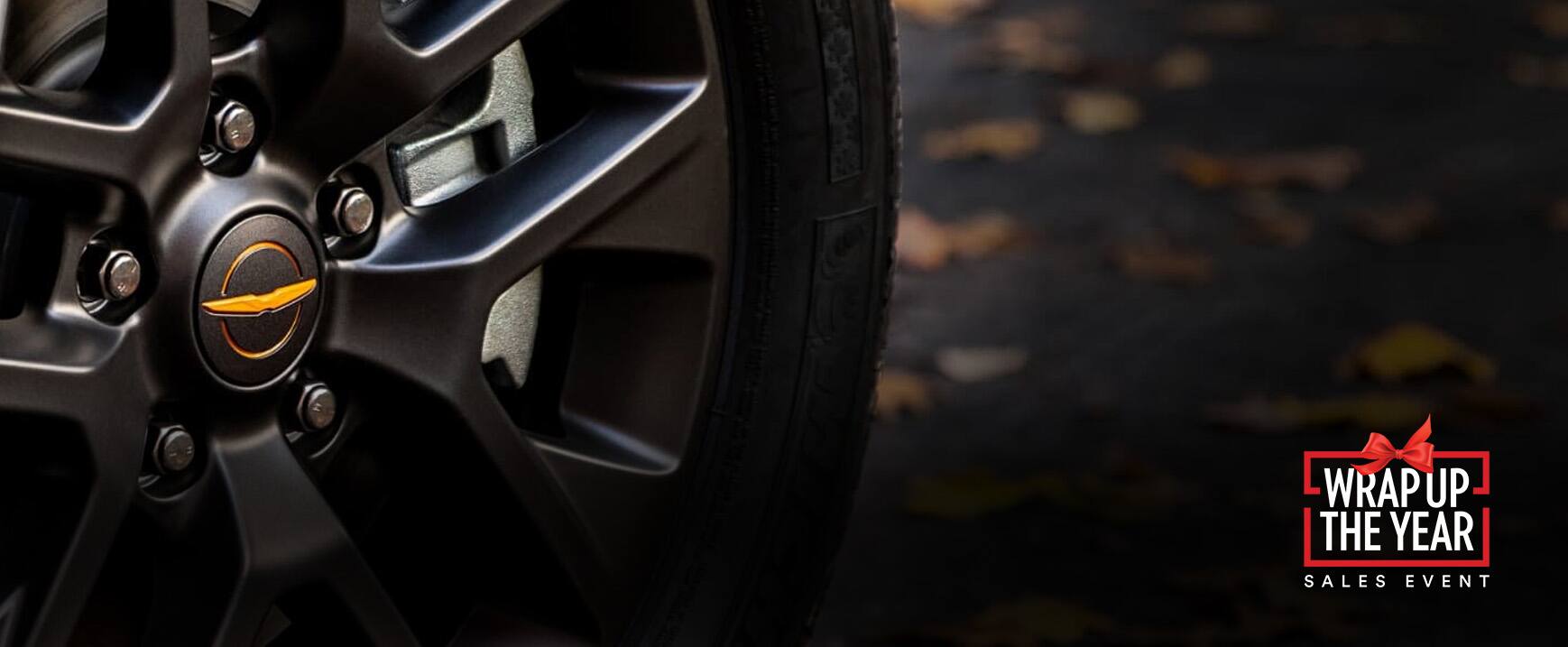 An extreme close-up of a wheel on the 2023 Chrysler Pacifica Road Tripper. Wrap up the year Sales Event logo.