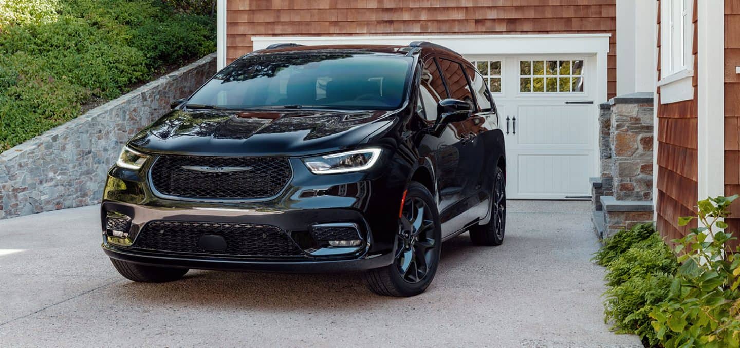Display A black 2024 Chrysler Pacifica Limited with S Appearance Package parked in the driveway of a contemporary home.