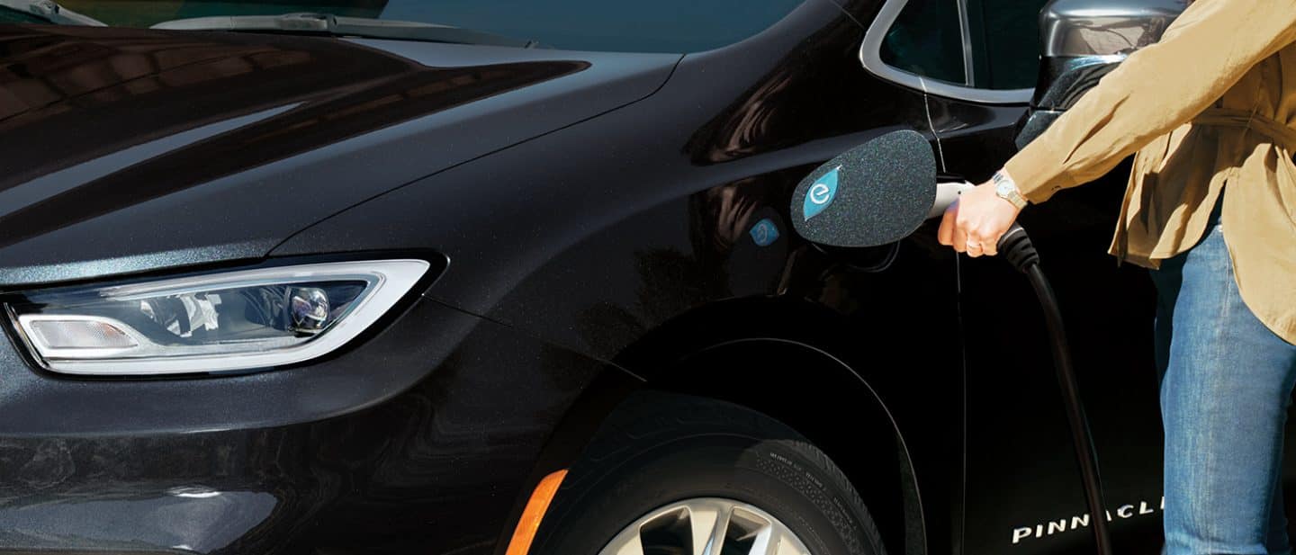 Display A 2024 Chrysler Pacifica Pinnacle Plug-In Hybrid with a charging cord being plugged into the vehicle's charging port.