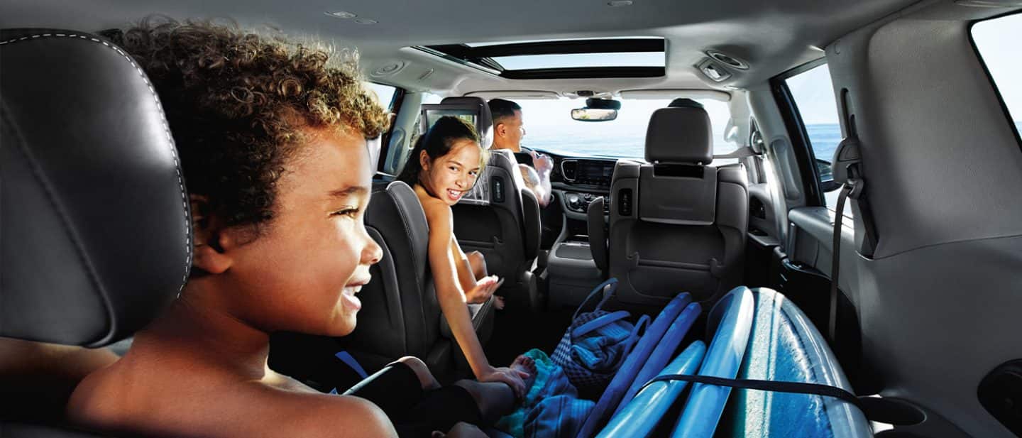  back seat interior view of a family and multiple surf boards in the 2024 Pacifica Hybrid driving to the beach