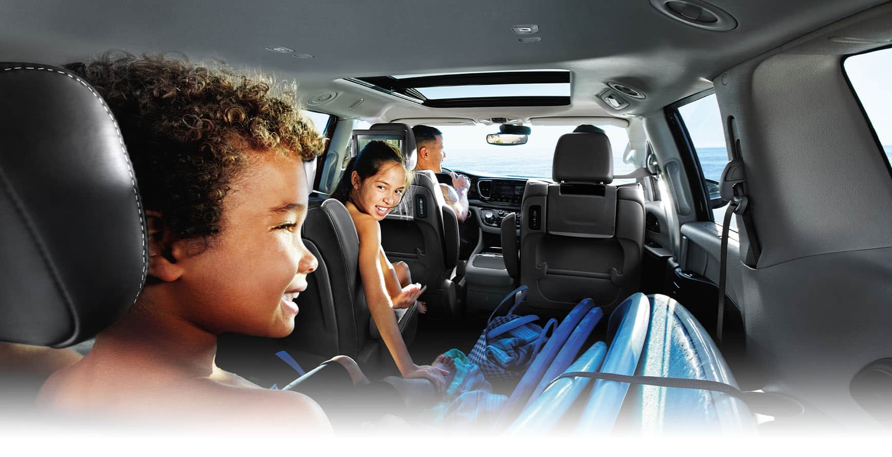 The interior of the 2024 Chrysler Pacifica Plug-In Hybrid from the rear of the vehicle, with a couple in the front seats, a child in the driver-side second-row seat, a child in the third-row seat and cargo on the floor of the passenger side.