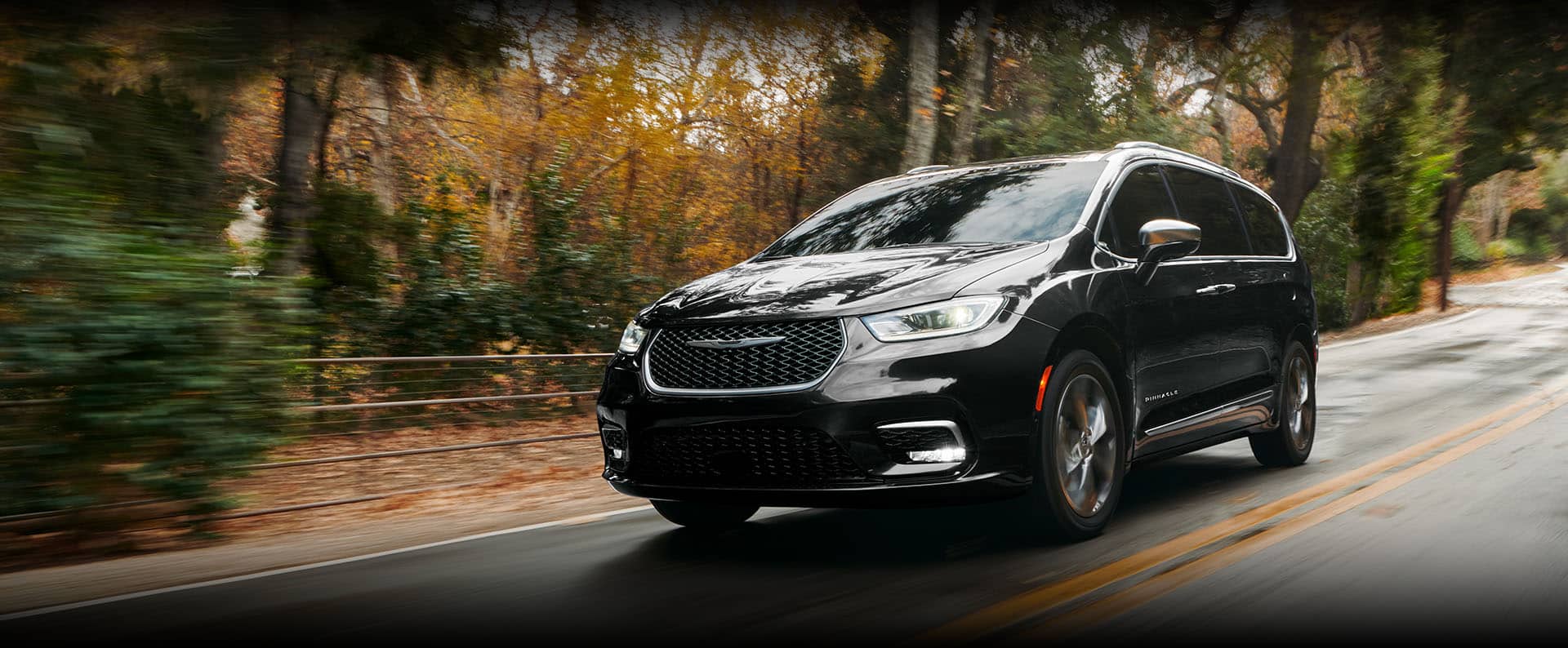 An angled driver-side profile of the 2024 Chrysler Pacifica Pinnacle being driven down a country road, the background is blurred to indicate the vehicle is in motion.