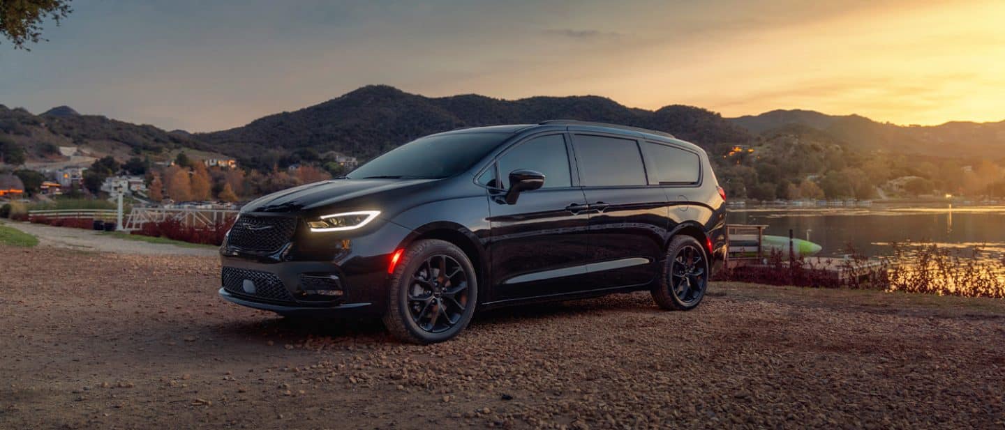 Display A black 2025 Chrysler Pacifica Limited parked by a lake at sunset.