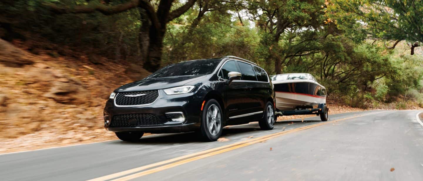 Display A black 2025 Chrysler Pacifica Pinnacle traveling down a highway, towing a motorboat. The background is blurred to indicate the vehicle is in motion.