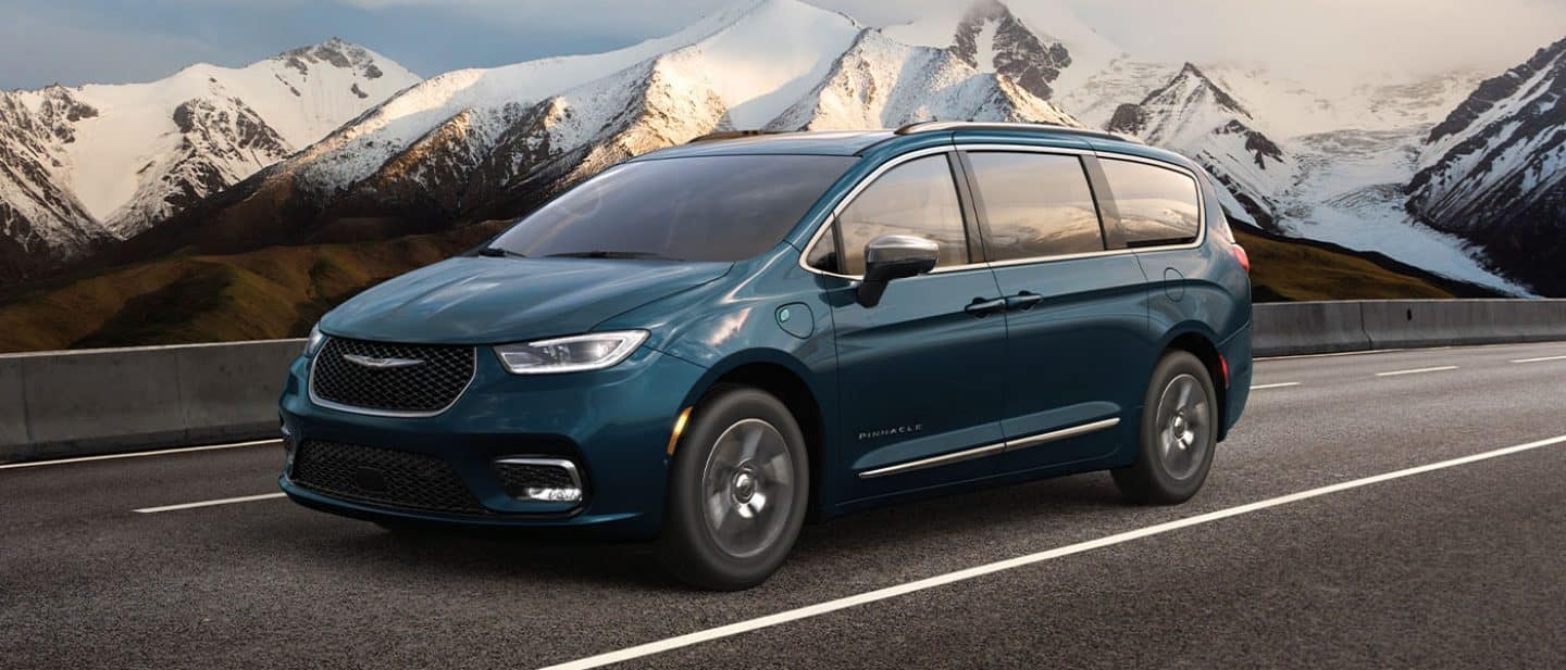 Display A blue 2025 Chrysler Pacifica Pinnacle Plug-in Hybrid being driven on a highway with mountains in the background.