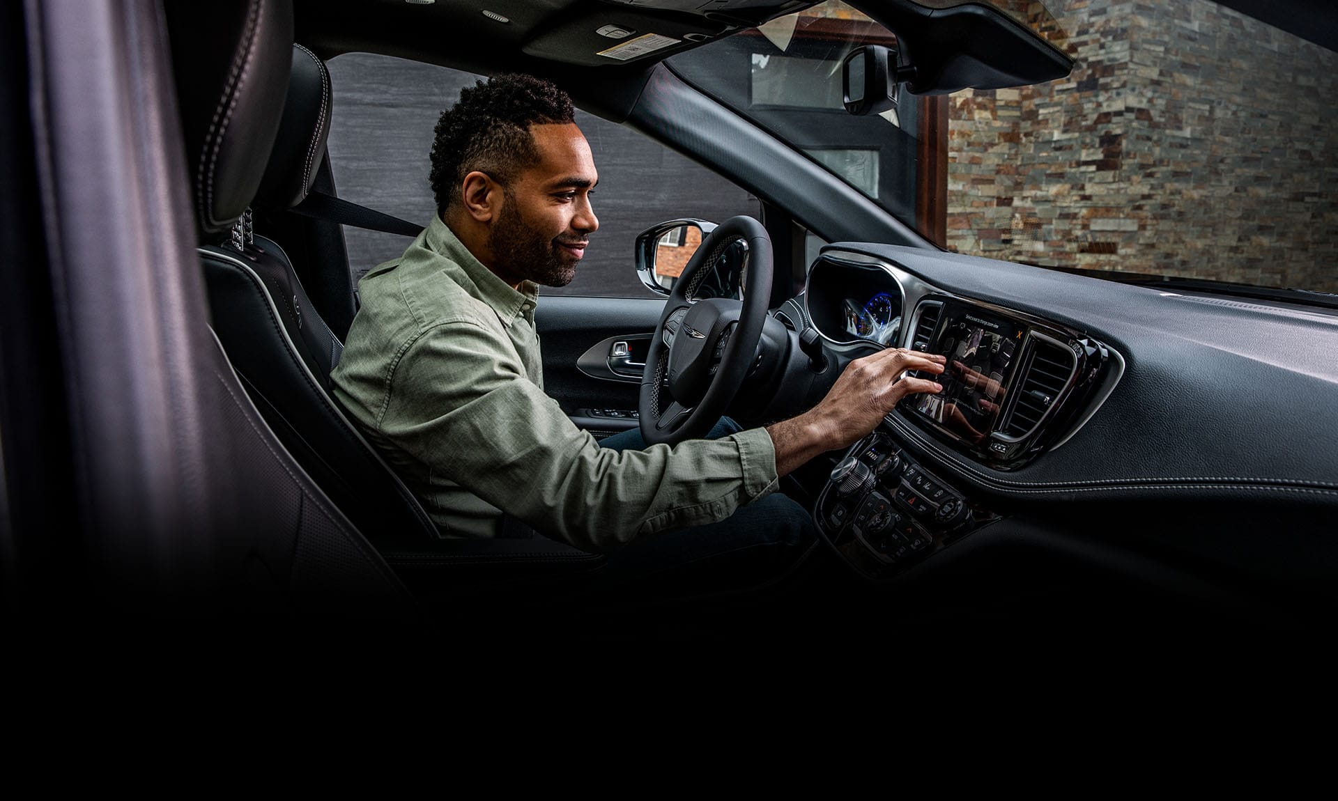 The front seat area in the 2025 Chrysler Pacifica Plug-in Hybrid with the driver making a selection on the Uconnect touchscreen.
