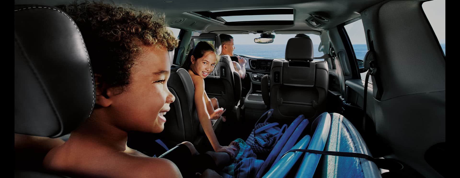 The interior of the 2025 Chrysler Pacifica Plug-in Hybrid from the rear of the vehicle, with a couple in the front seats, a child in the driver-side second-row seat, a child in the driver-side third-row seat and cargo on the second- and third-row passenger side.