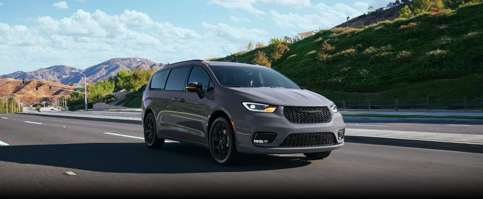 A light gray 2025 Chrysler Pacifica Limited traveling down a highway in the mountains.