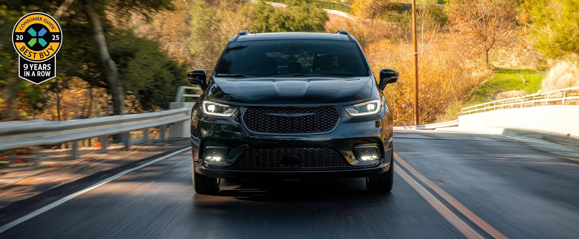 A front angle of a black 2025 Chrysler Pacifica Limited traveling down a highway. The background is blurred to indicate the vehicle is in motion.