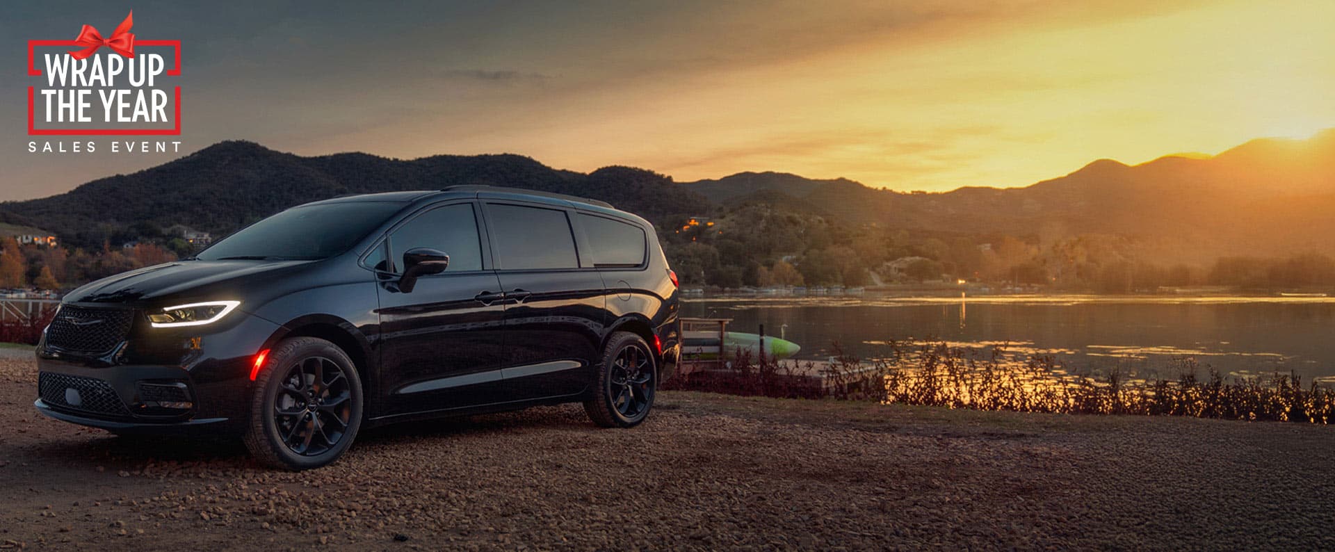 A black 2025 Chrysler Pacifica Limited parked by a lake at sunset. Employee Pricing Plus sales event. Wrap Up the Year Sales Event.