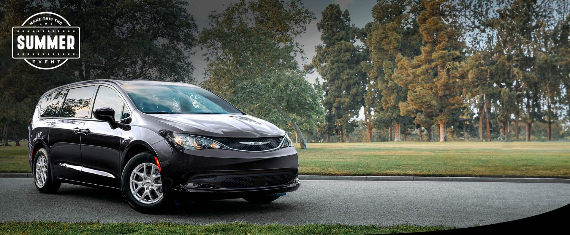 A front pasengers side view of a black 2025 Chrysler Voyager LX in a parking lot of a park. Make this the Summer sales event.