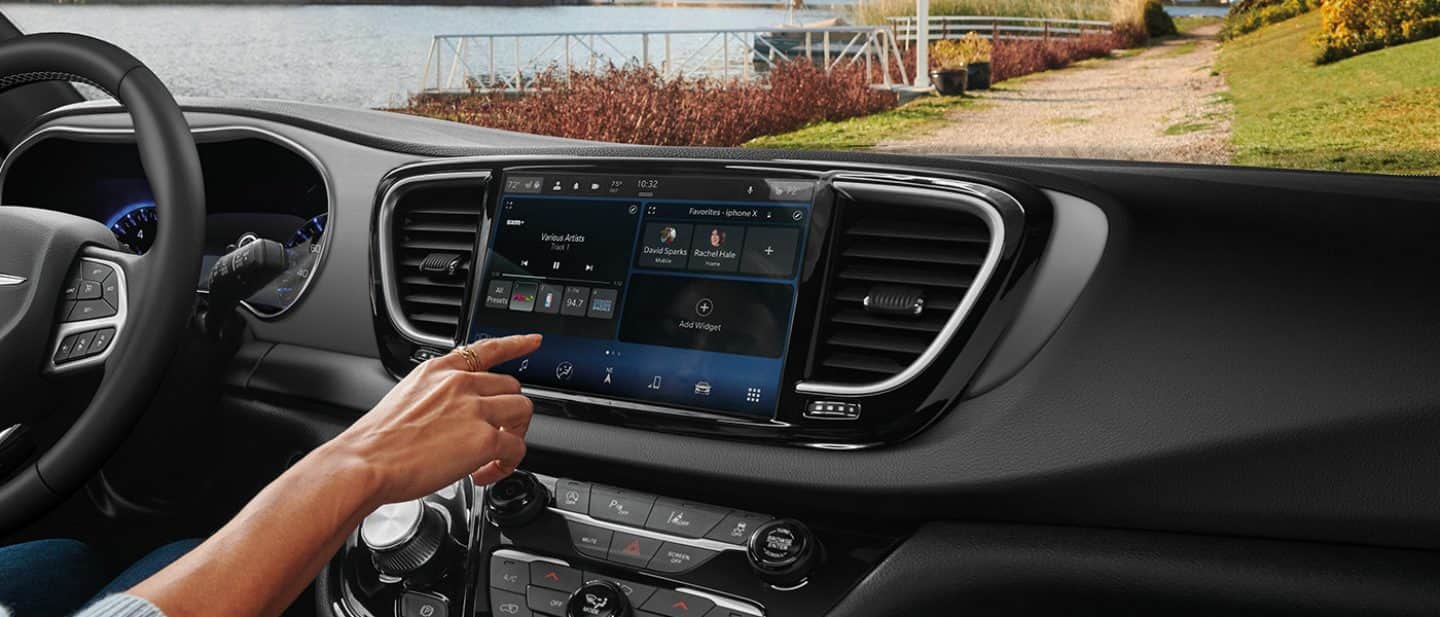 Display A female driver in a 2025 Chrysler Voyager LX making a music selection on the Uconnect touchscreen.