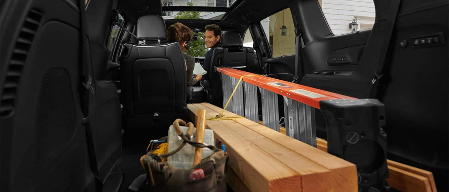 Display The interior of the 2026 Chrysler Pacifica with the third-row and one of the second-row Stow n Go seats folded into the floor, in order to accommodate a ladder and long pieces of lumber.