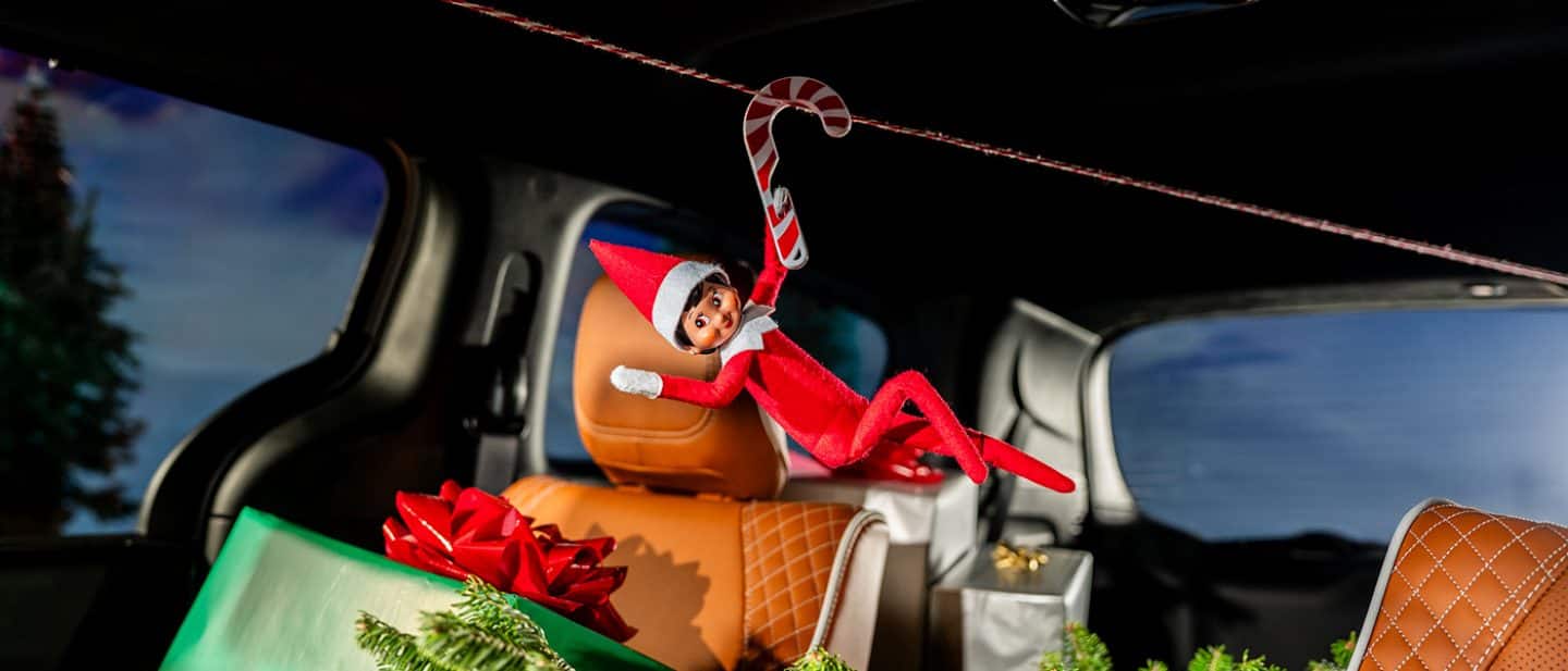 Display Sparkles, the Elf on the Shelf holding a candy cane that's hanging on a string across the interior of a 2026 Chrysler Pacifica Pinnacle, with holiday gifts and decorations in the cargo area and on the second-row seats.