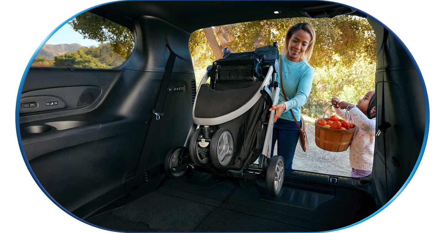 A  woman pulling a collapsed stroller out of the cargo area of a 2026 Chrysler Pacifica Hybrid.