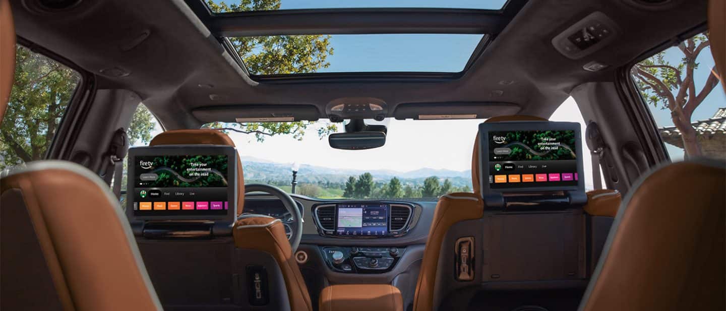 Display The interior of the 2026 Chrysler Pacifica Plug-in Hybrid Pinnacle, with the open dual-pane sunroof and the two seatback-mounted touchscreens in the second row, all shot from the third row.