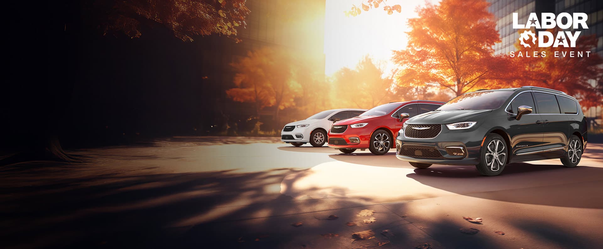 Three 2026 Chrysler minivan models parked on an oceanside beach. From left to right: a white Chrysler Voyager, a blue Pacifica Pinnacle Plug-in Hybrid and a red Pacifica Pinnacle. Labor day Sales Event.