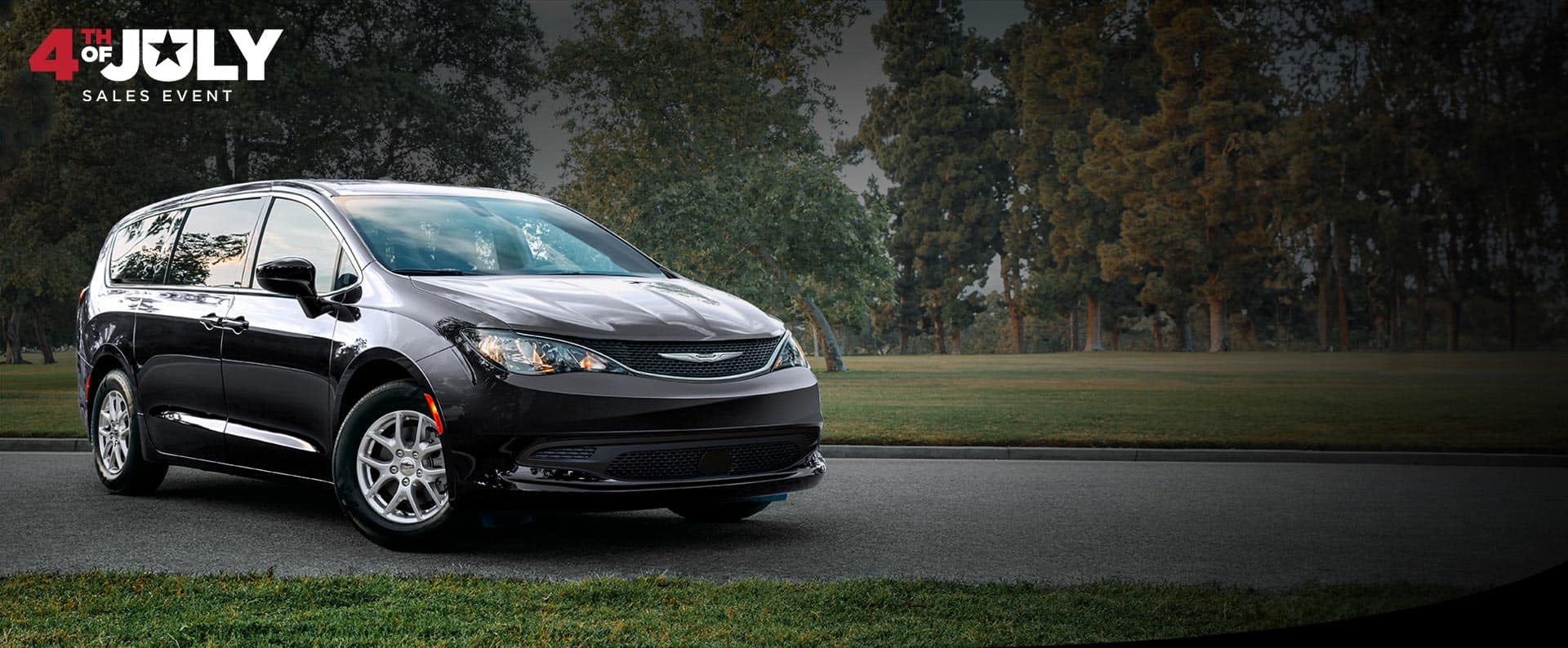 A front passengers side view of a black 2026 Chrysler Voyager LX in a parking lot of a park. 4th of July Sales Event.