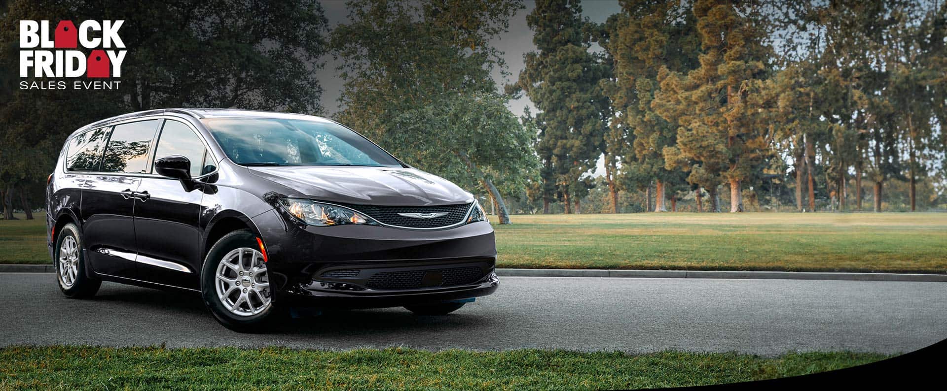 A front passengers side view of a black 2025 Chrysler Voyager LX in a parking lot of a park. Black Friday Sales Event.