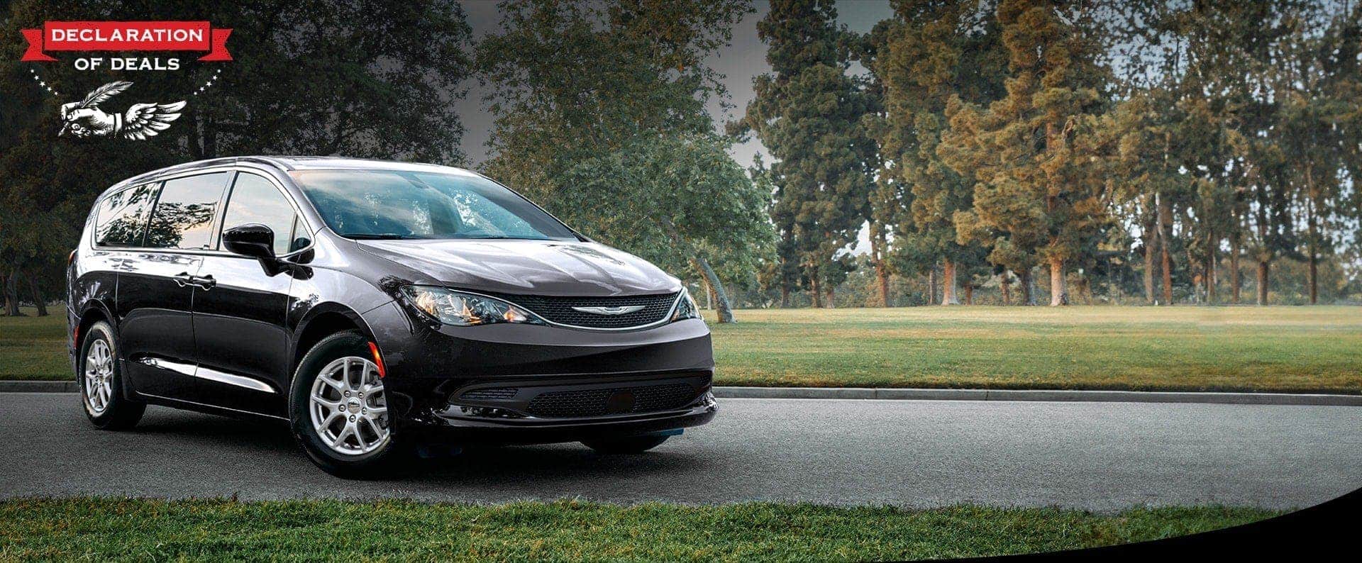 A front passengers side view of a black 2026 Chrysler Voyager LX in a parking lot of a park. Declaration of Deals Sales Event.